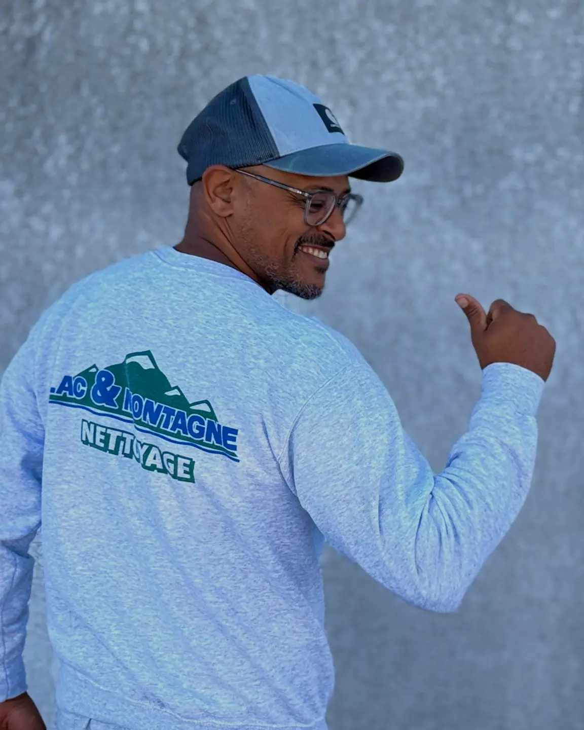 Un agent en sweat Lac & Montagne Nettoyage montre du pouce, en souriant, le logo dans son dos