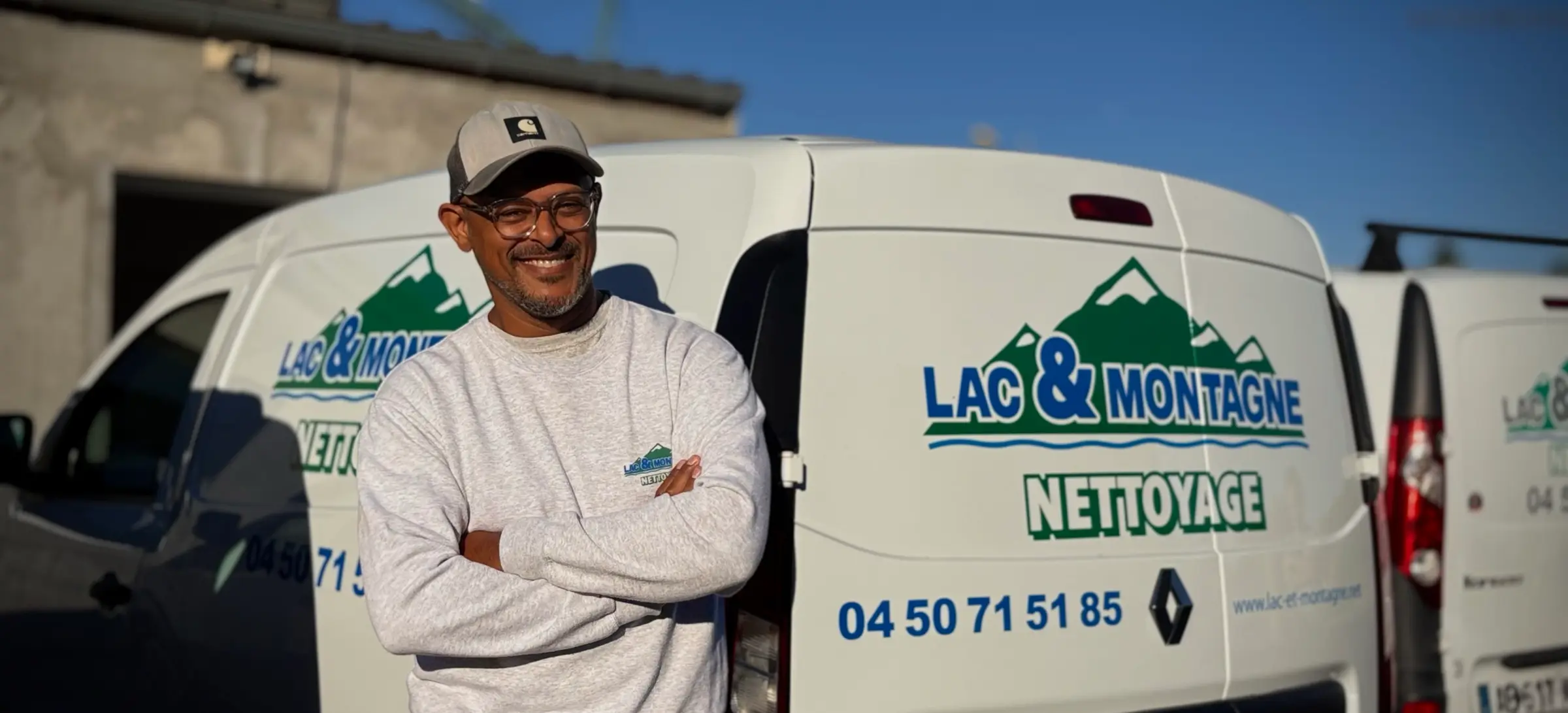 Un agent de Lac & Montagne Nettoyage, bras croisés et souriant, devant les camionnettes de l’entreprise